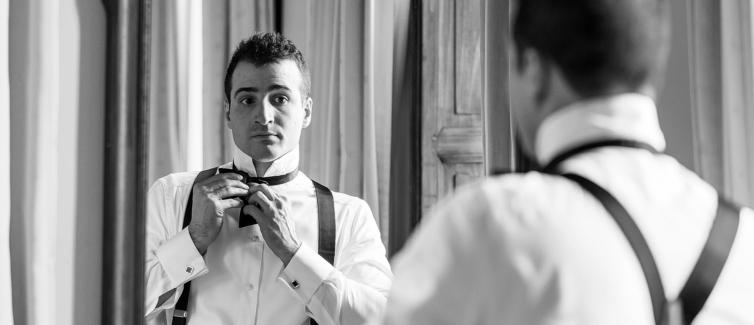 Man adjusting bow tie in mirror reflection