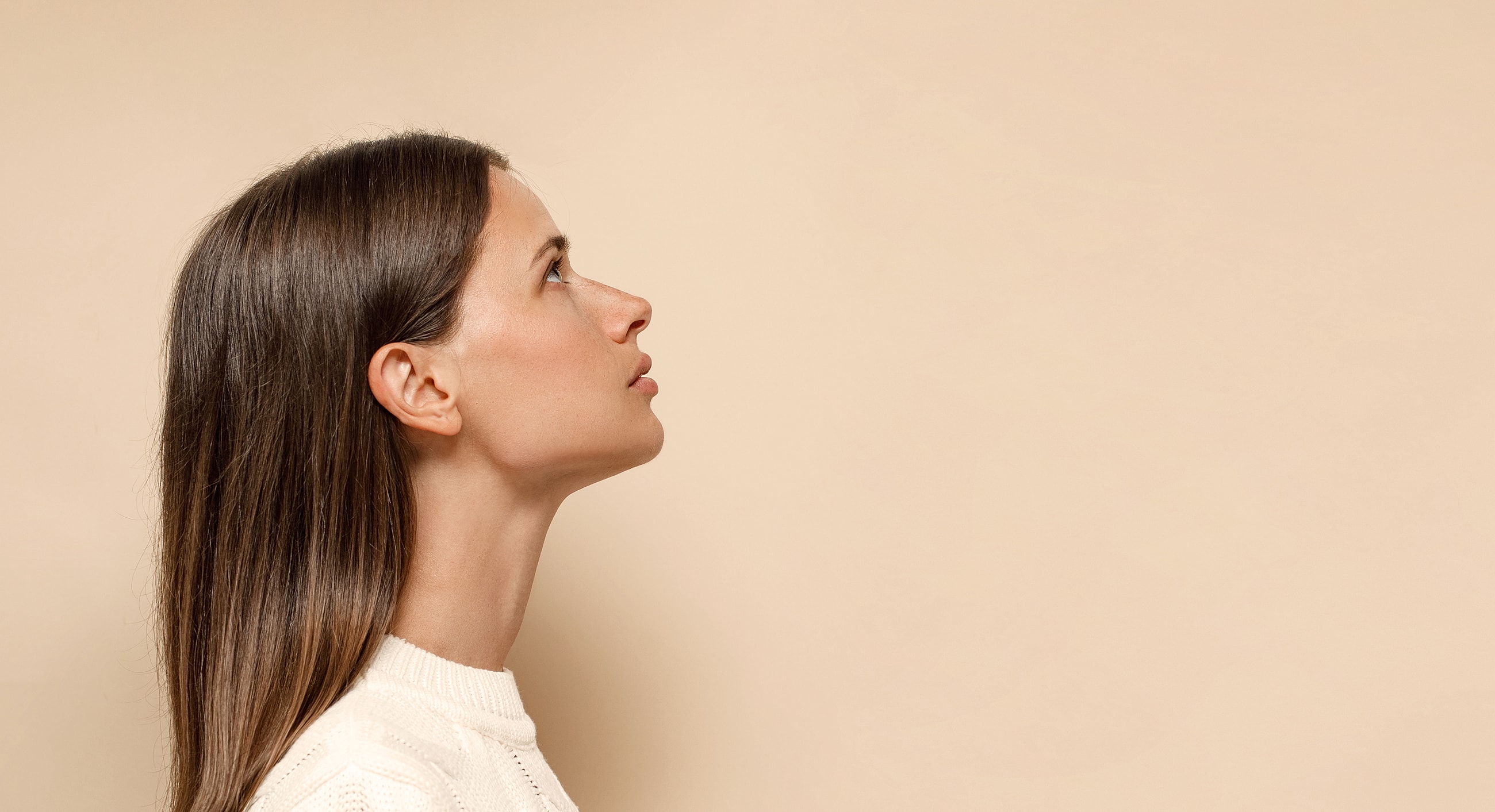 Profile of a woman looking upward against beige background.